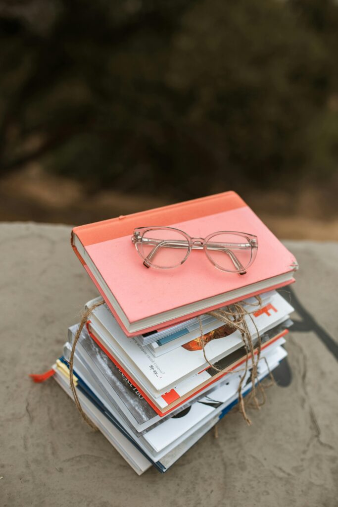 A stack of assorted books with eyeglasses placed on top, captured outdoors.